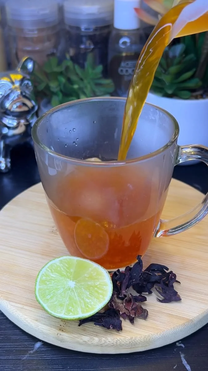 Infusión servida en una taza de vidrio junto a limón y flores secas
